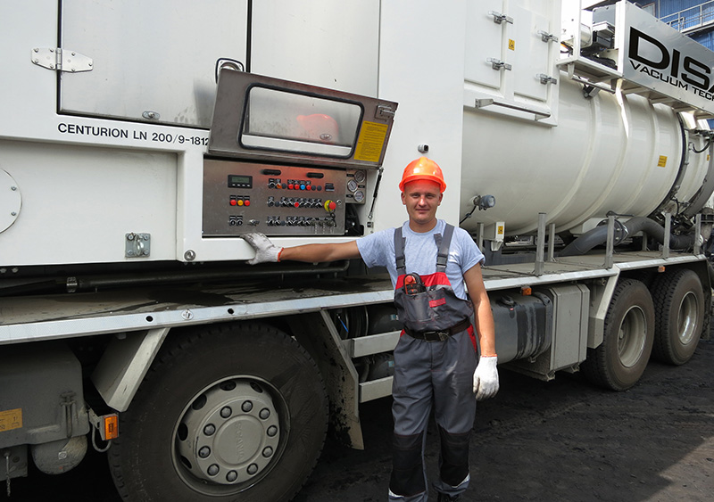 Operator in safety gear standing beside a DISAB Centurion™ LN10 vacuum truck, interacting with the external control panel used to manage the vacuum and pressure tank system.