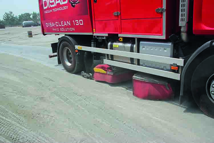 Red DISA-CLEAN street sweeper in operation on a dry dirt-covered surface, using advanced vacuum technology to remove fine dust particles without water.