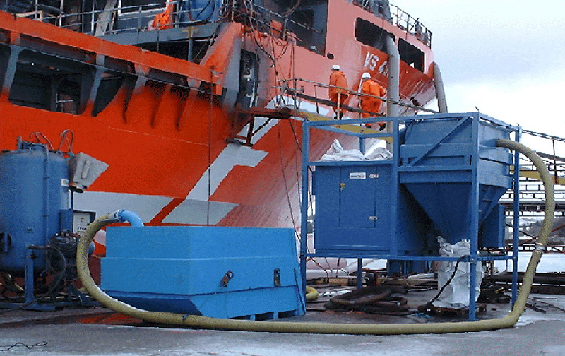 Blue DISAB SEBF-III industrial vacuum unit set up dockside next to a large vessel, connected via heavy-duty suction hoses, highlighting its flexibility and capability for both dry and wet material handling in marine or offshore environments.