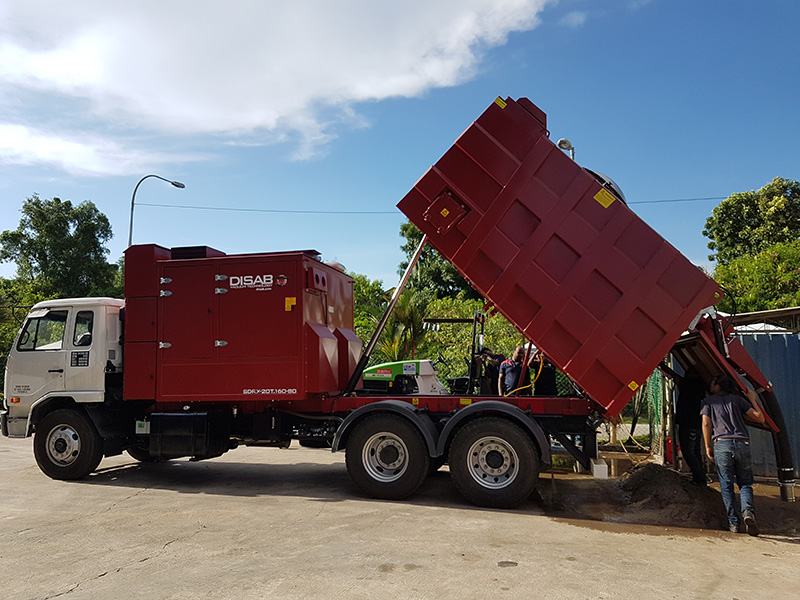 Red DISAB TrailerVAC industrial vacuum truck parked outside a large processing facility, showcasing its mobility and ability to handle dust and material extraction in complex industrial environments.