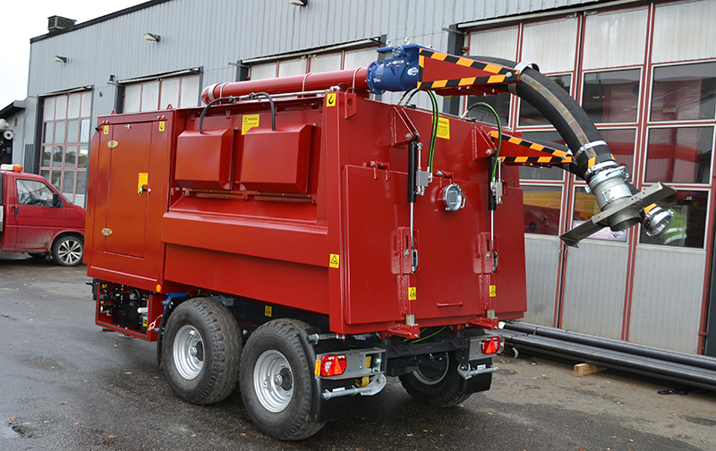 Red DISAB TrailerVAC SDT-10T unit parked outside a factory building, featuring a raised suction hose and control cabinet, ready for industrial vacuum tasks involving dust and material recovery.