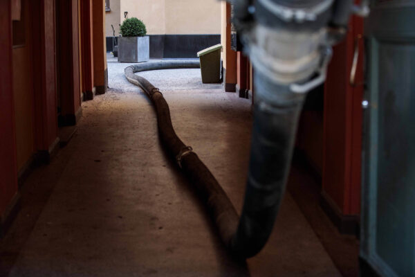 DISAB vacuum hose extended through an open-air corridor between buildings, showing the system’s long reach and adaptability for accessing hard-to-reach industrial cleaning zones.
