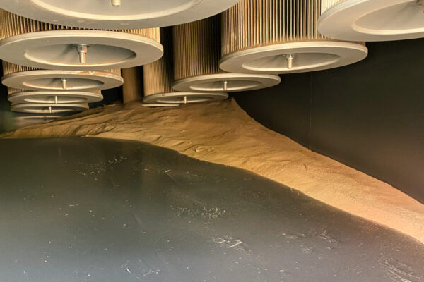 Interior of DISAB industrial vacuum chamber where cylindrical cartridge filters hang above a mound of collected sand‑dust.