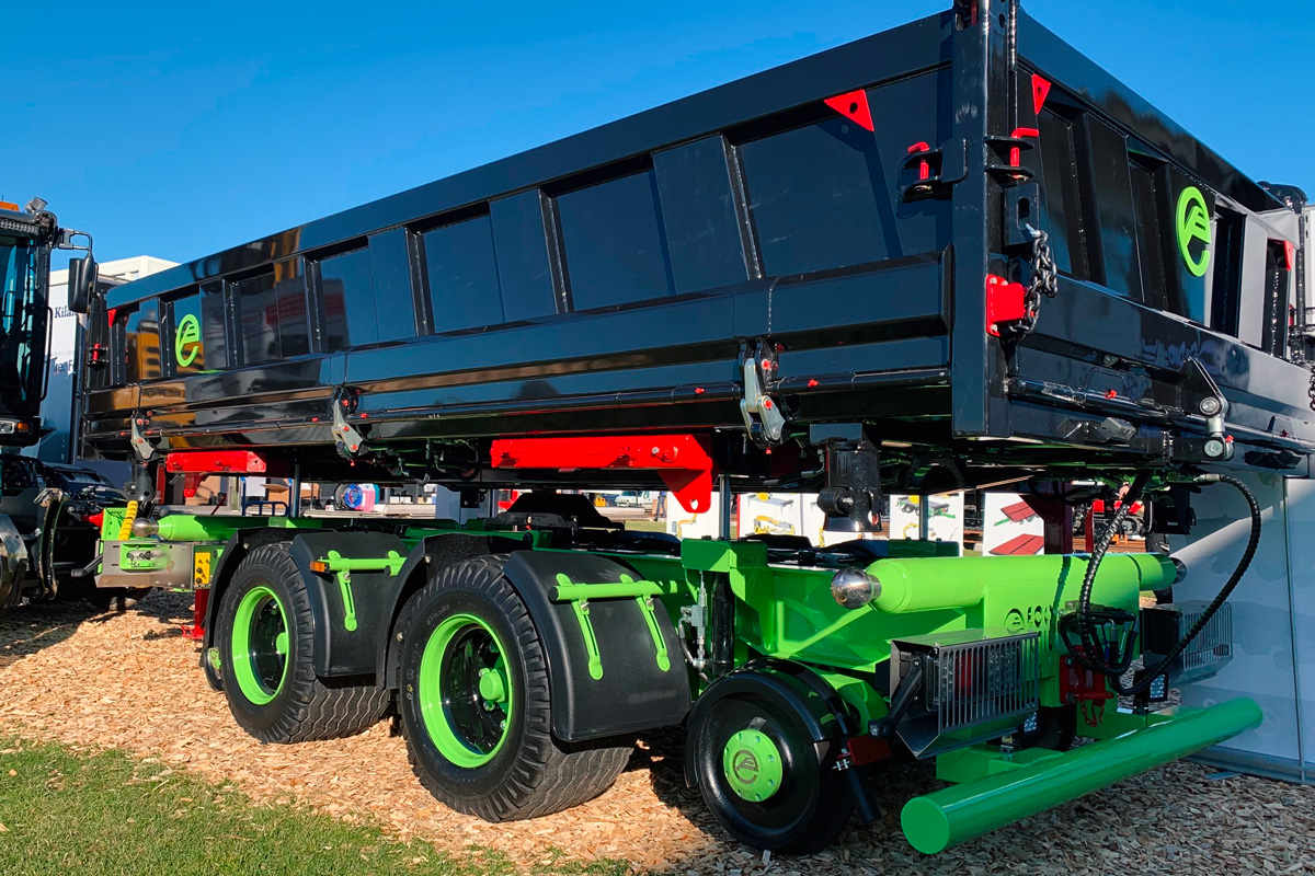 DISAB two‑axle vacuum loader trailer with glossy black tipping container and bright‑green chassis on display against clear blue sky.
