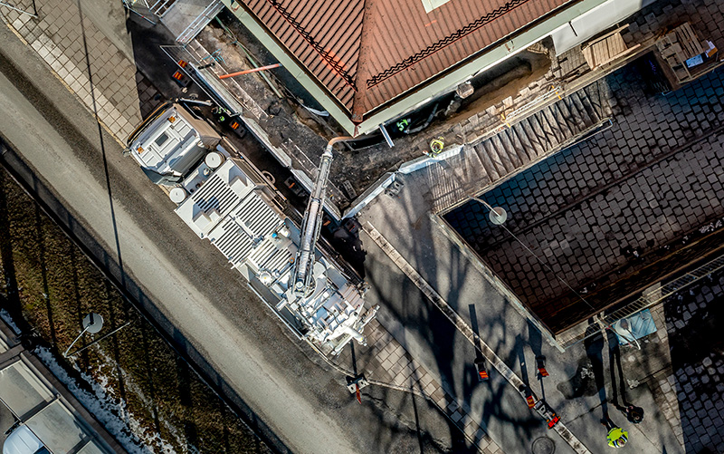 Aerial view of DISAB Centurion™ LN10RR vacuum unit in operation on a city street, connected by hoses and supported by a hooklift truck, demonstrating its flexibility and use in urban environments.