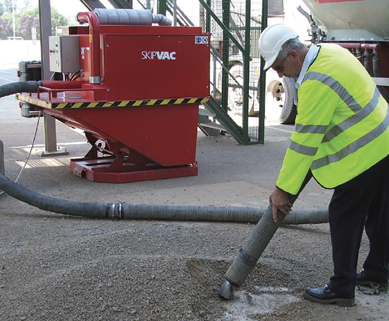 Worker in high-visibility clothing using the DISAB SkipVAC vacuum system to clean up spilled material on an outdoor industrial site, demonstrating its effectiveness in improving workplace cleanliness and safety.
