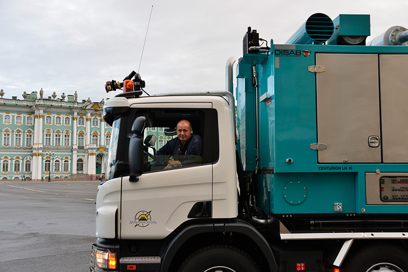Blue DISAB Centurion™ LN10 vacuum unit mounted on a truck chassis, parked near a historic city building, showcasing its mobility and adaptability for industrial suction tasks in urban environments.